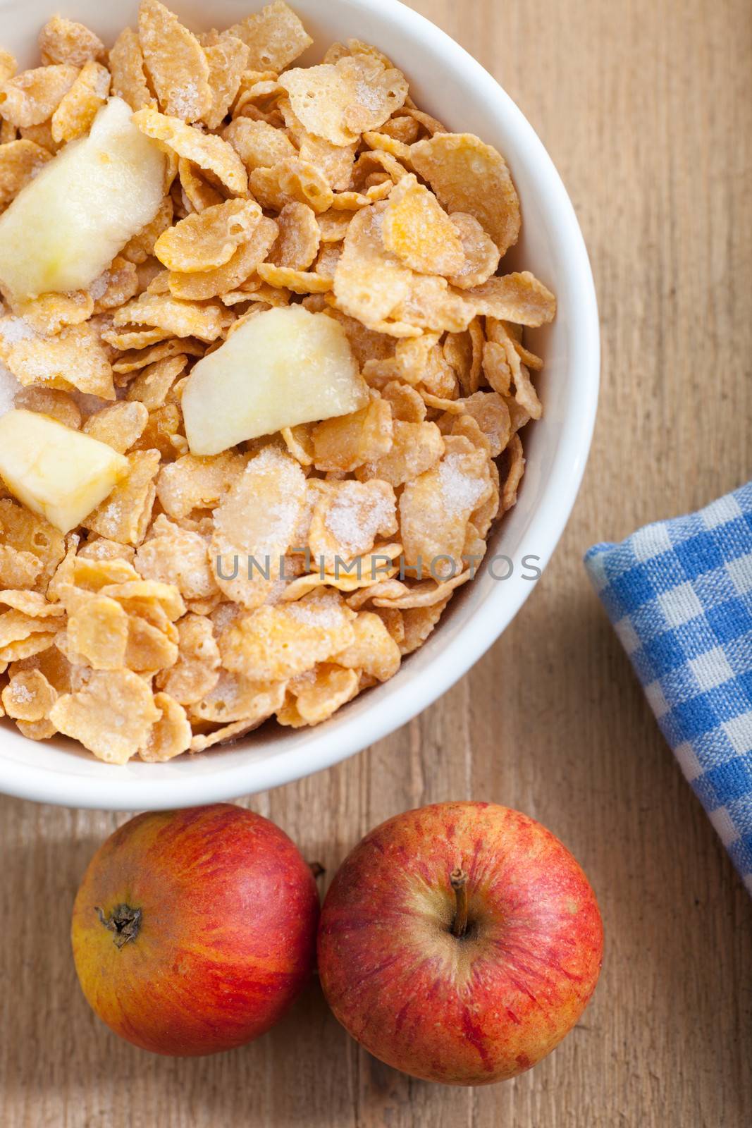 Overhead view of a healthy breakfast of fresh corn flakes cereal served with chopped fruit in a bowl and two fresh red apples