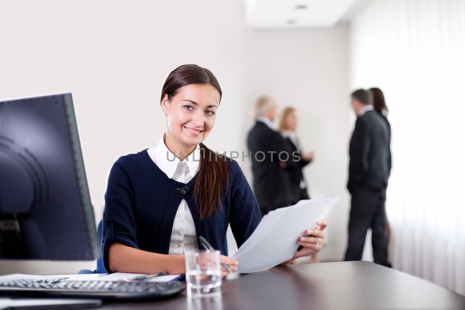 Closeup portrait of happy young business woman holding important office documents and smiling at the camera with colleagues