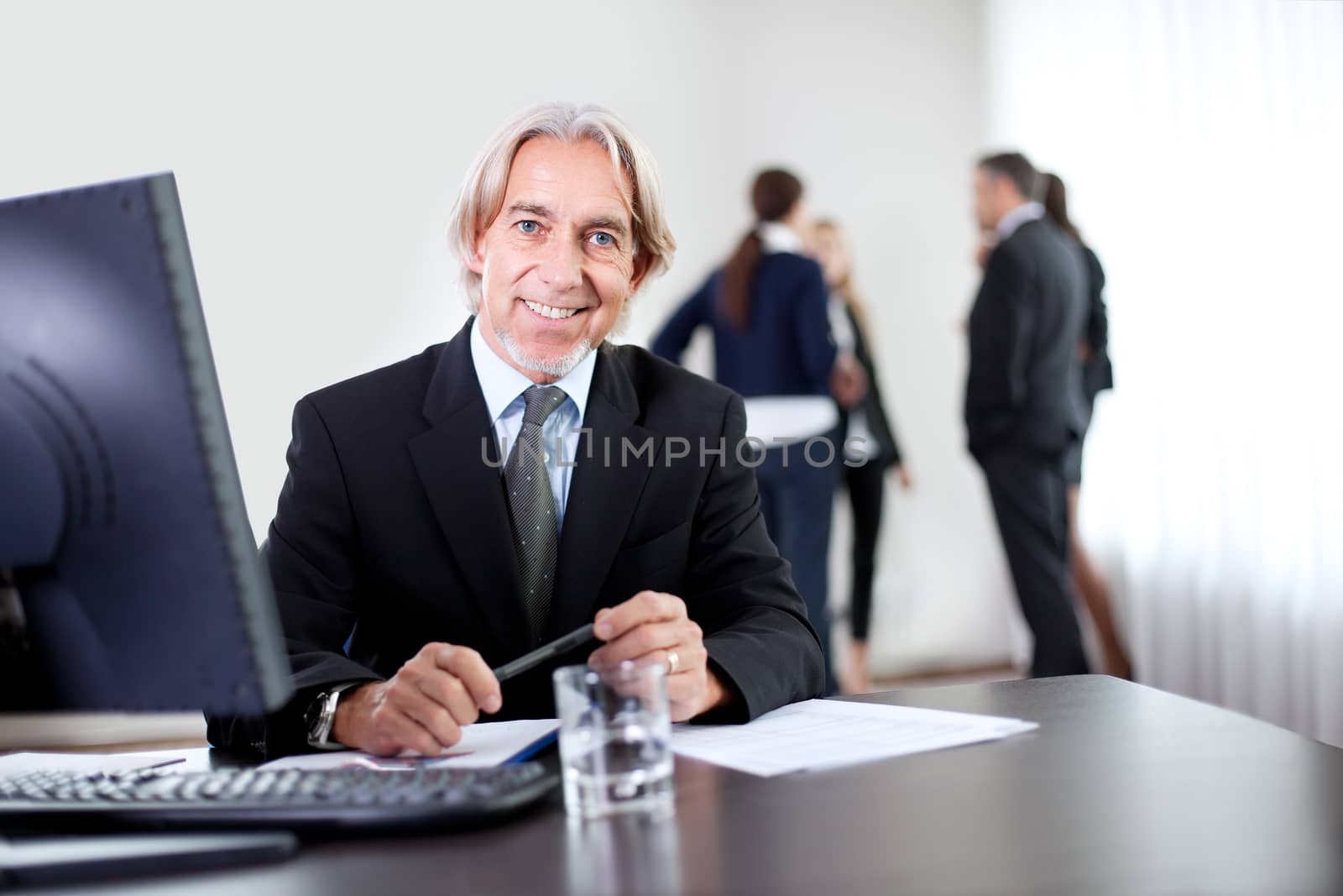 Closeup portrait of satisfied confident businessman sitting at his office with colleagues chatting in the background