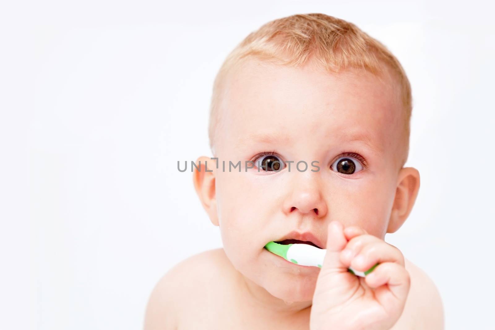 Cute baby brushing his teeth and looking at the camera on white background