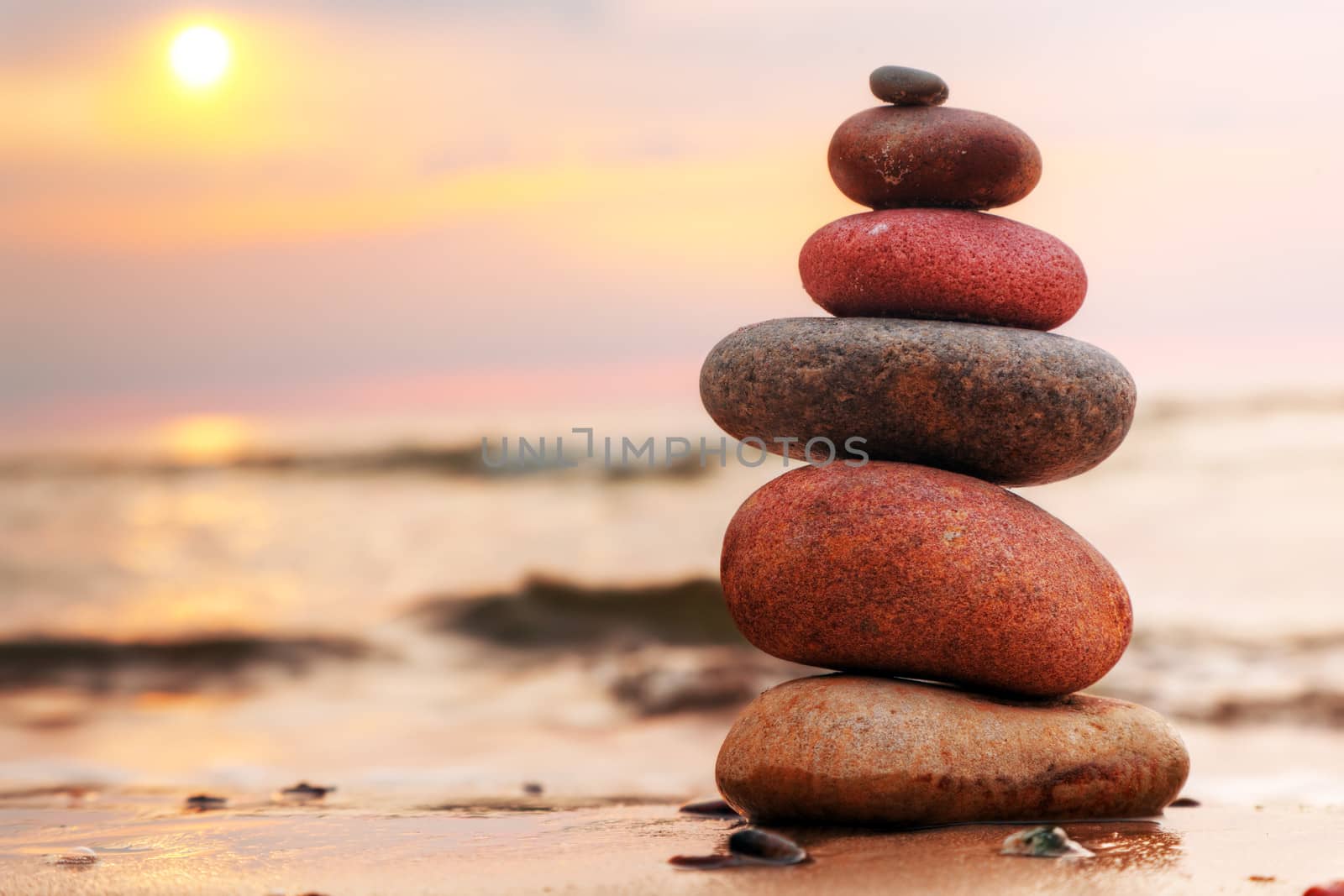 Stones pyramid on sand symbolizing zen, harmony, balance. Ocean at sunset in the background