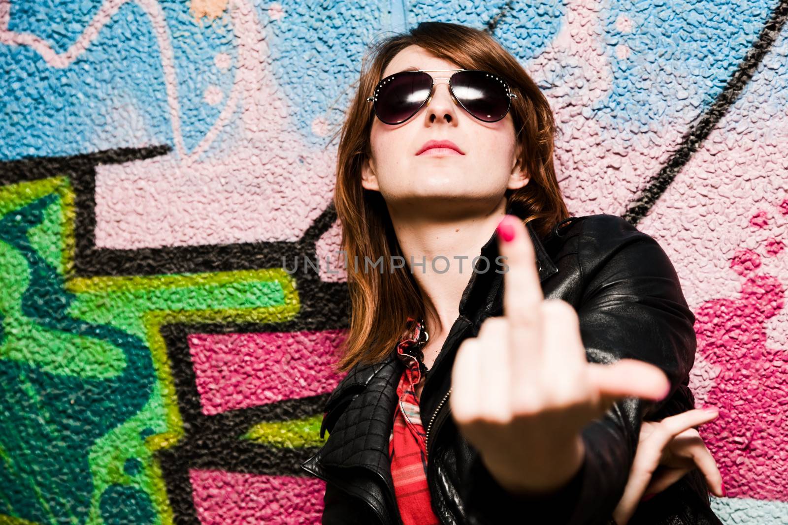 Stylish fashionable girl showing fuck off middle finger gesture against colorful graffiti wall.
