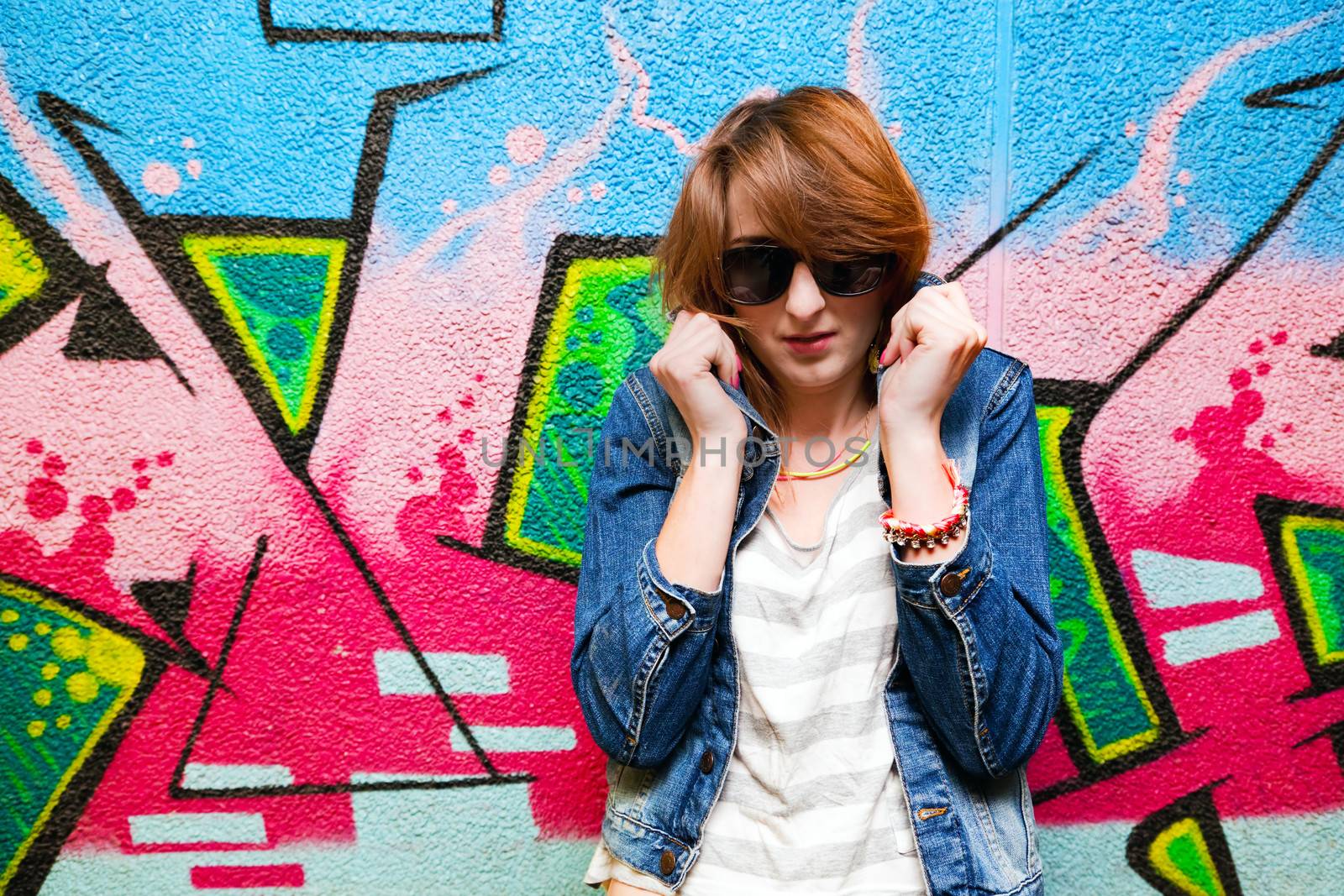 Stylish fashionable girl in jeans jacket portrait against colorful graffiti wall. Fashion, trends, subculture.