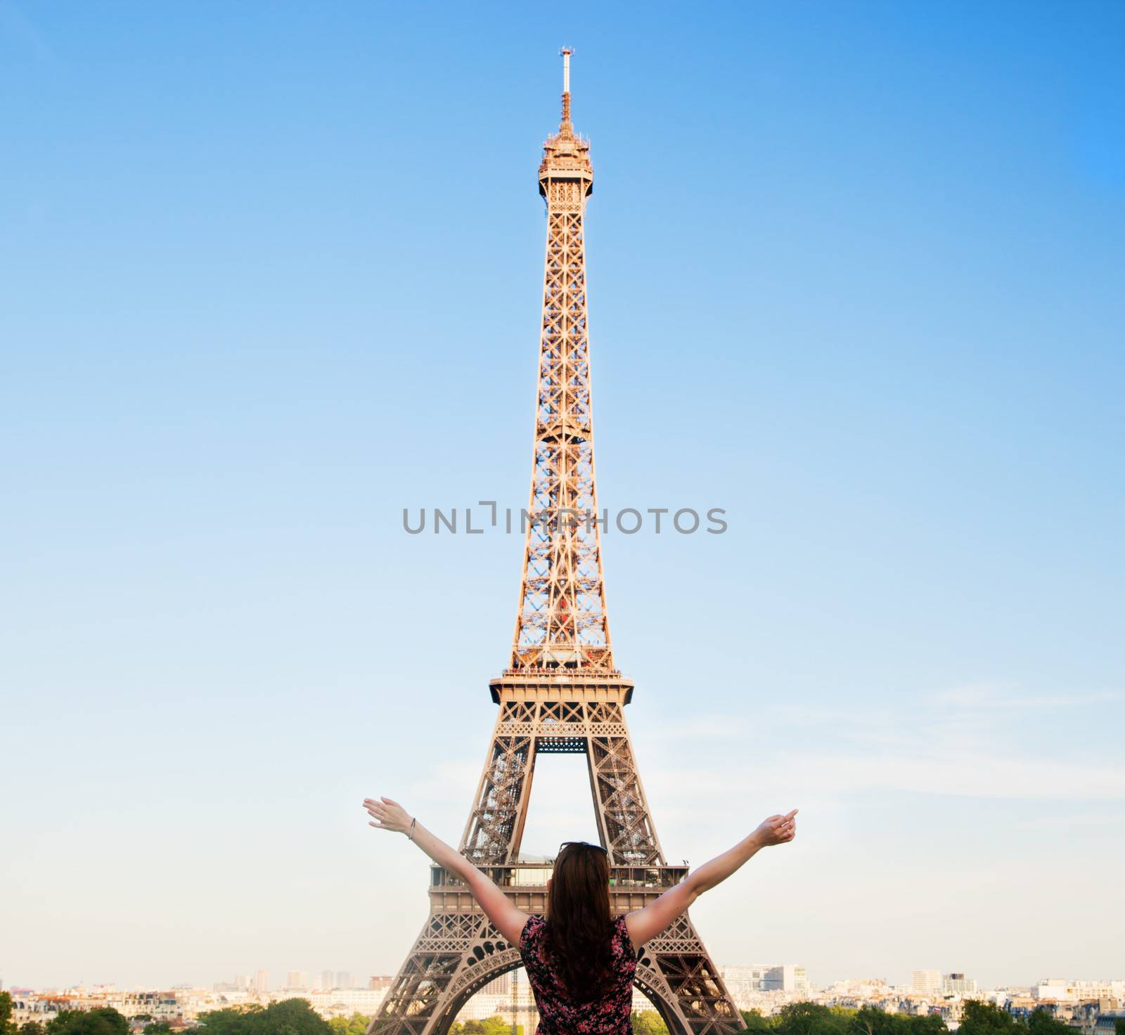Young attractive happy woman with hands up facing the Eiffel Tower in Paris, France