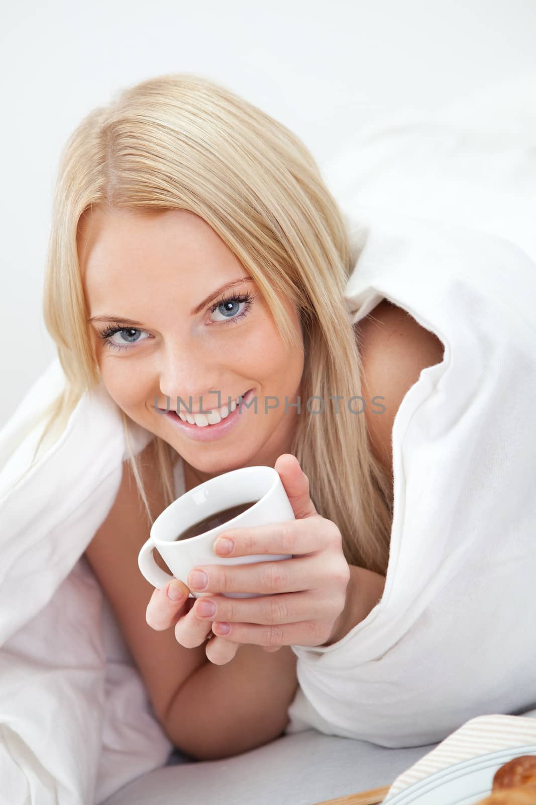 Beautiful woman drinking coffee in bed while eating breakfast