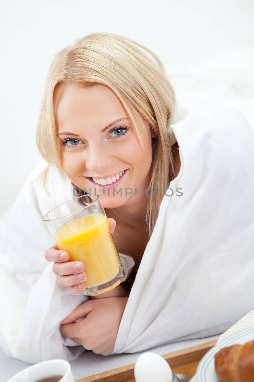 Beautiful woman drinking juice in bed while eating breakfast