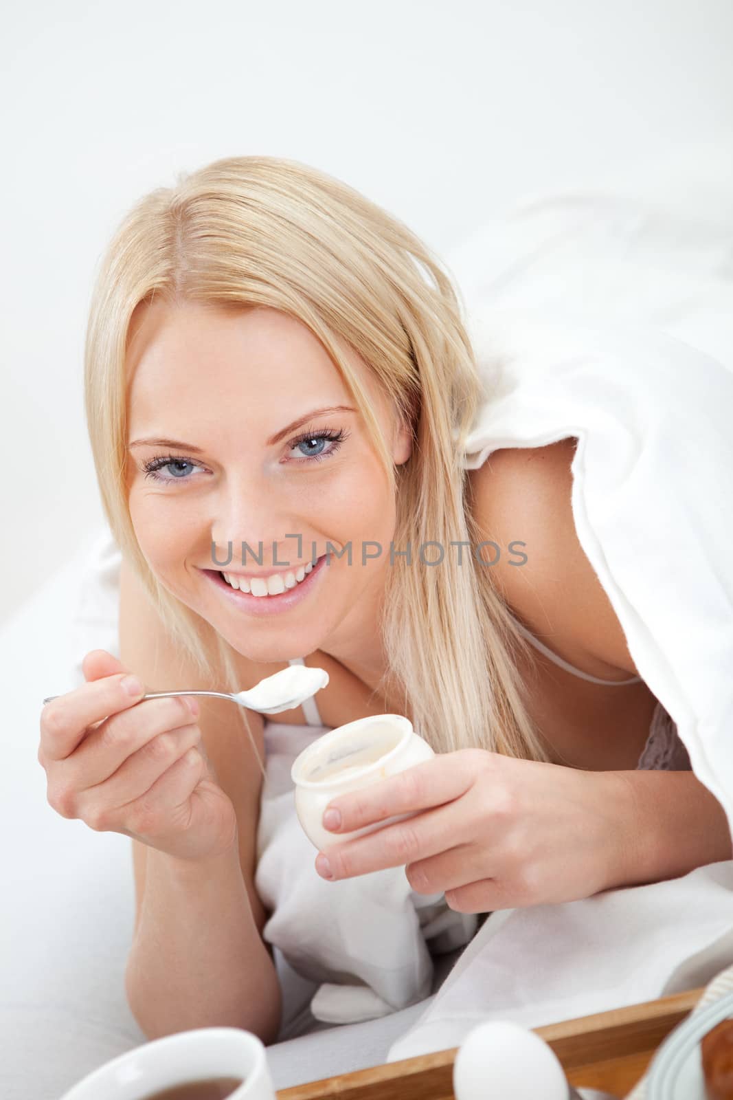 Beautiful woman eating yogurt in bed during the breakfast