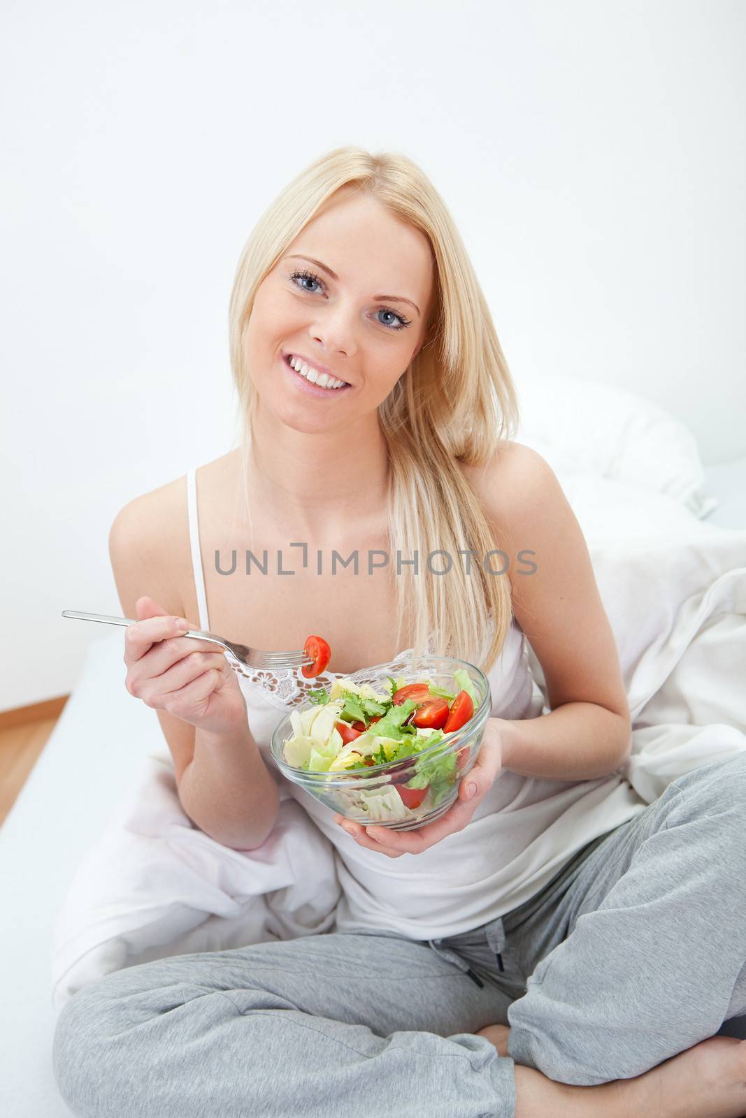 Beautiful woman eating green salad in bed