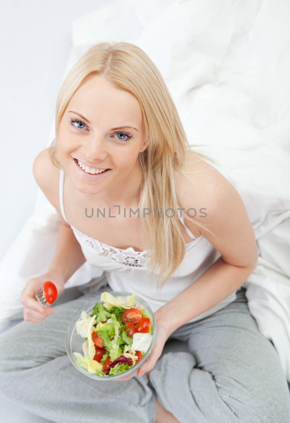 Beautiful woman eating green salad in bed