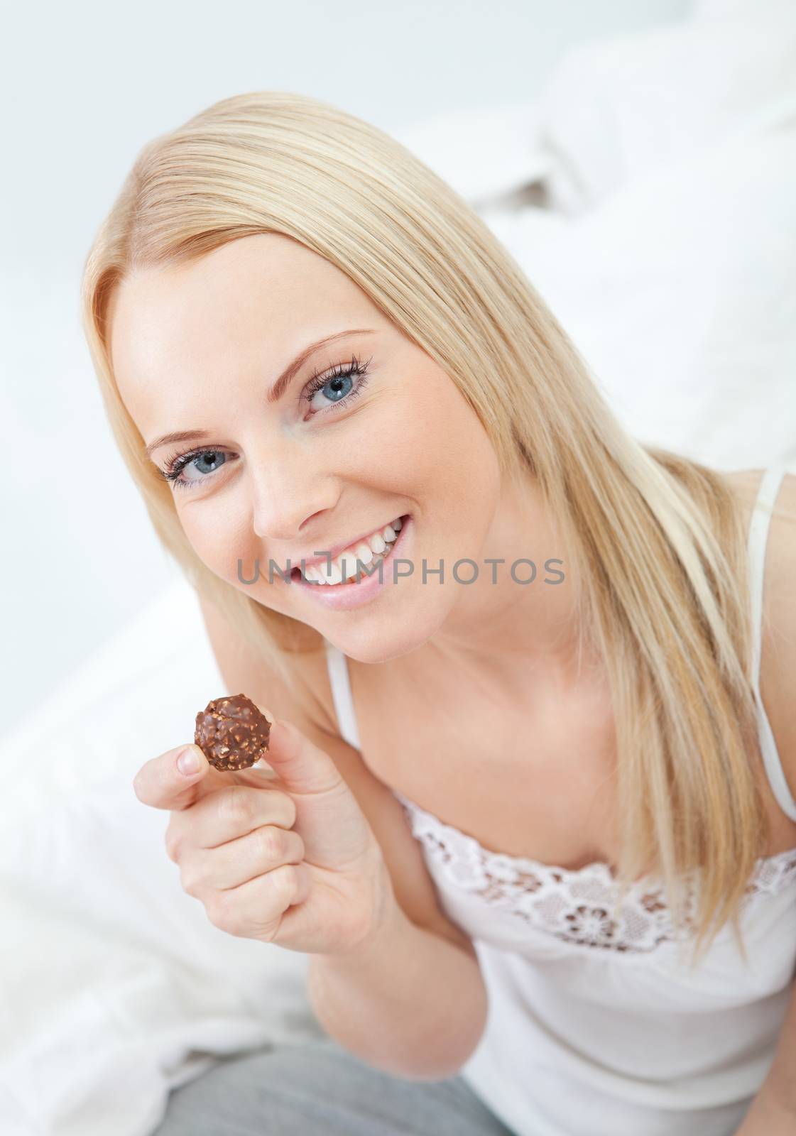 Beautiful young woman eating chocolate in bed
