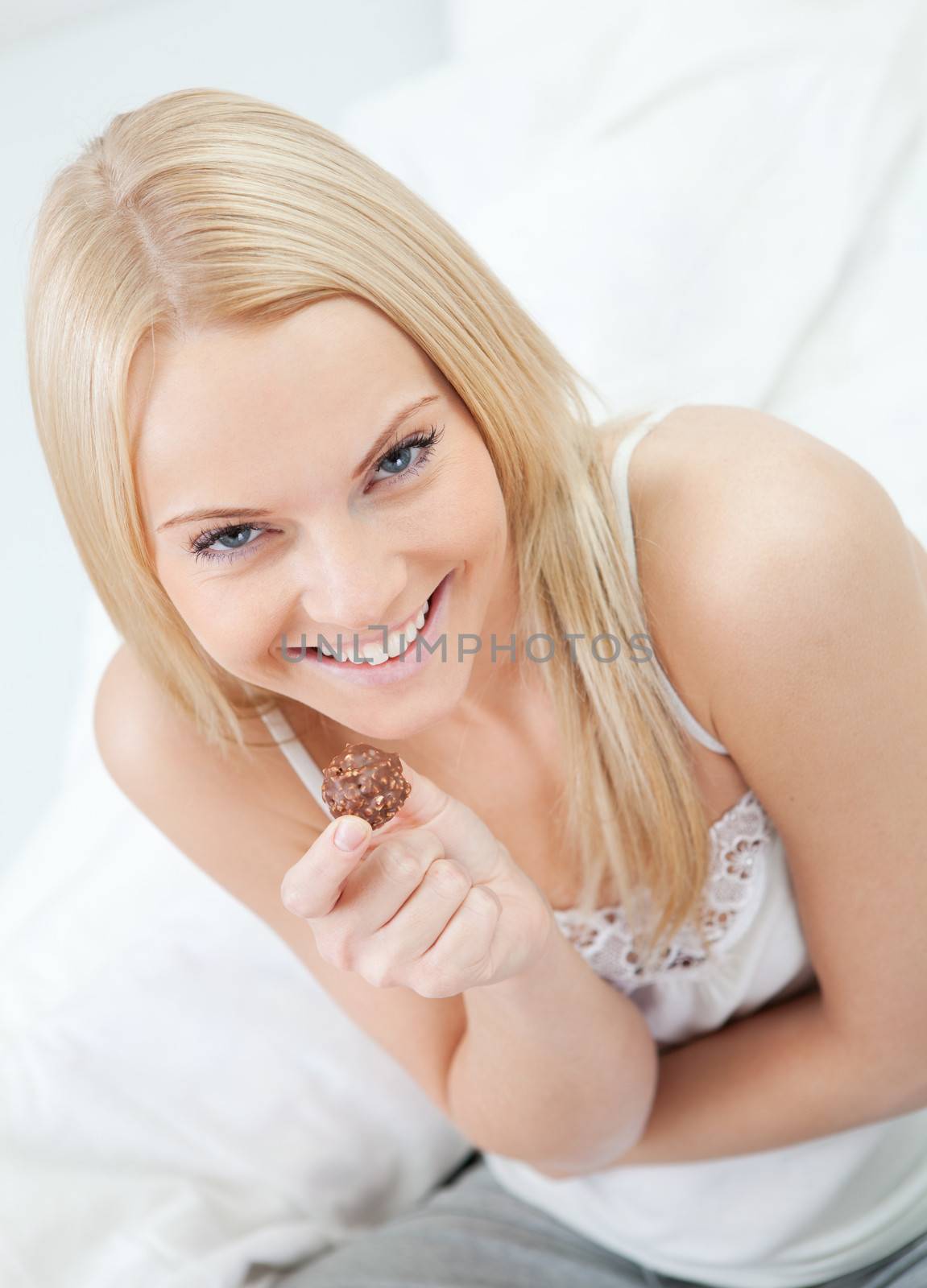 Beautiful young woman eating chocolate in bed