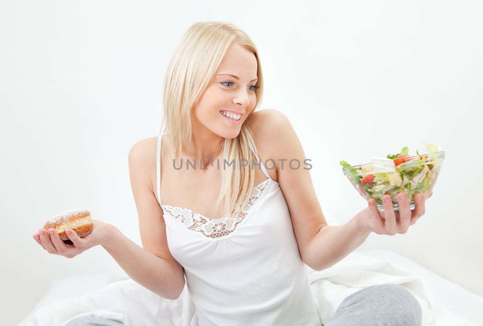 Tempted young woman making a choice between salad and donut