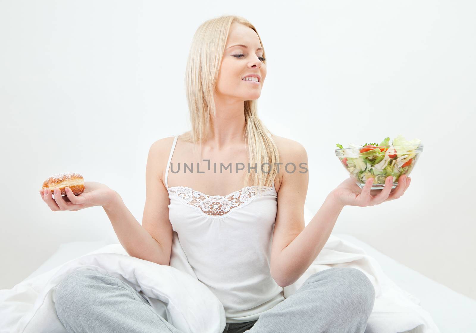 Tempted young woman making a choice between salad and donut