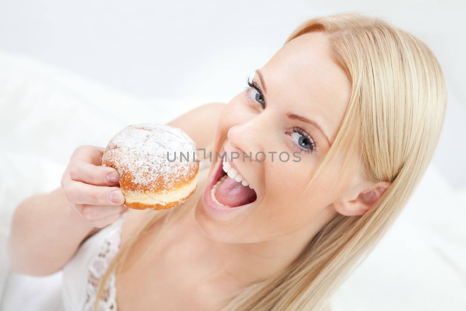 Beautiful woman eating tasty donut in bed