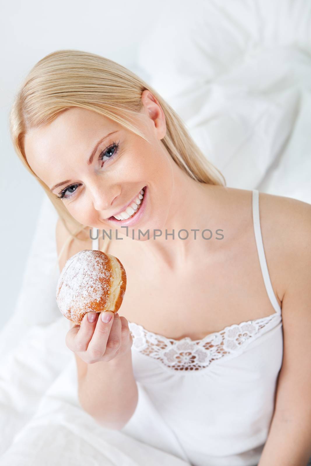 Beautiful woman eating tasty donut in bed