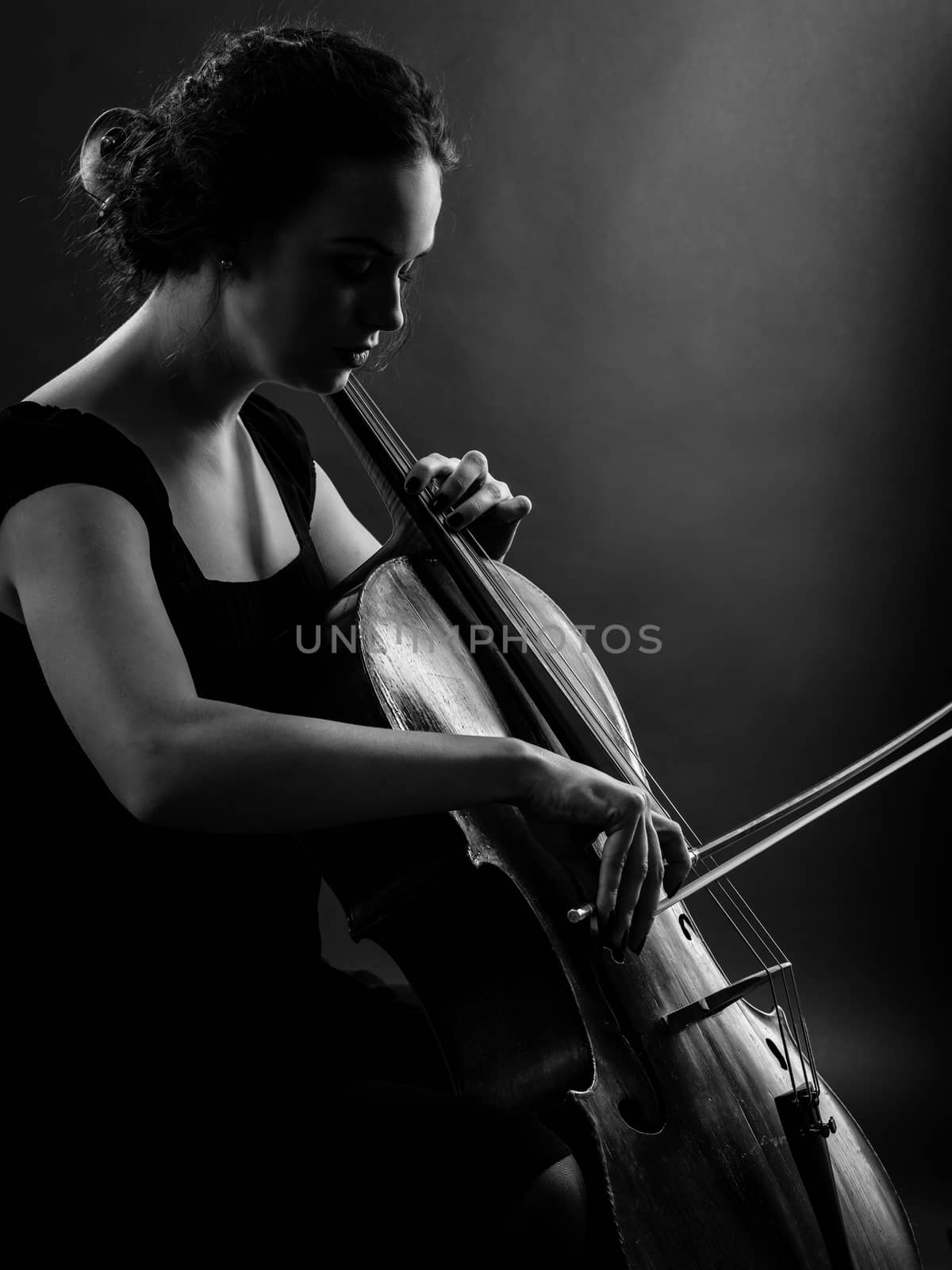 Photo of a beautiful female musician playing a cello. Backlit black and white image.
