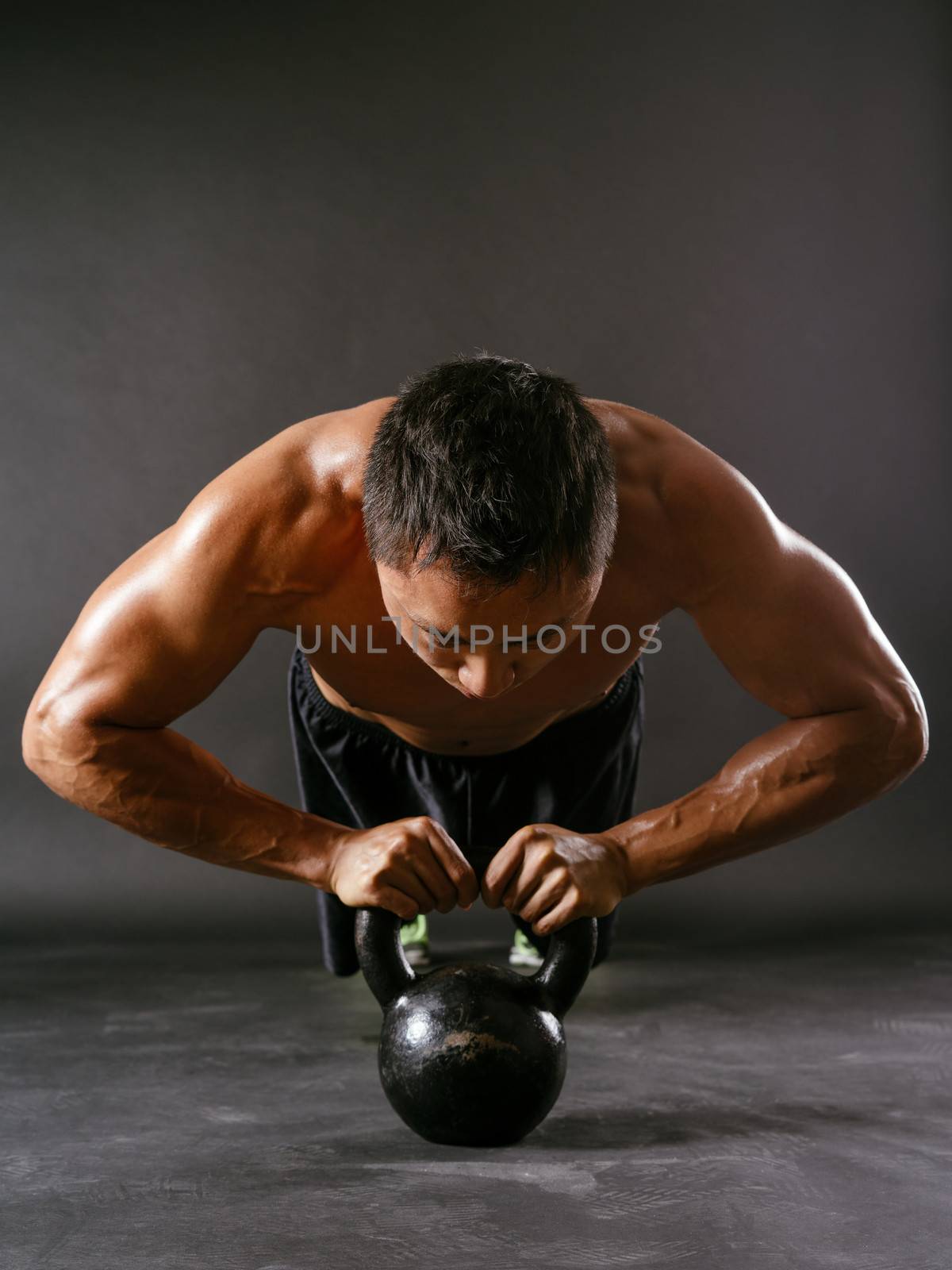 Photo of a muscular Asian man doing pushups with a kettlebell.
