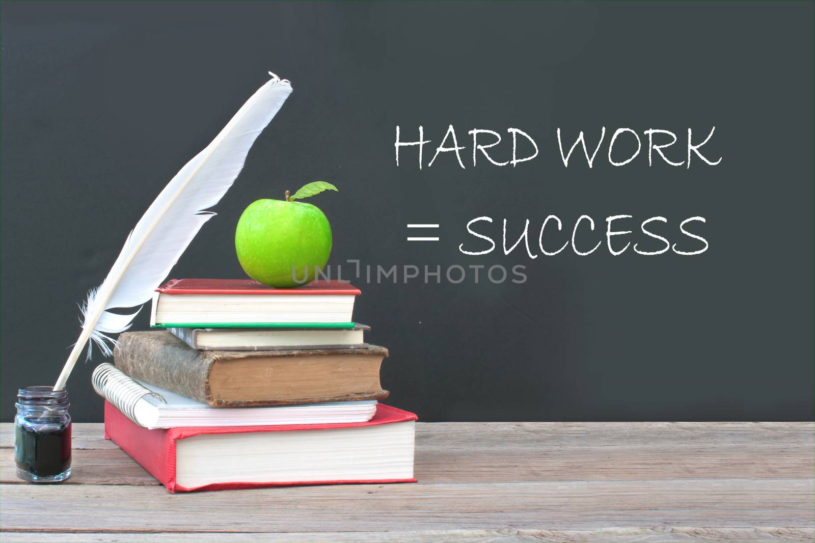 Hard work is success written on a blackboard with a pile of books, quill and ink