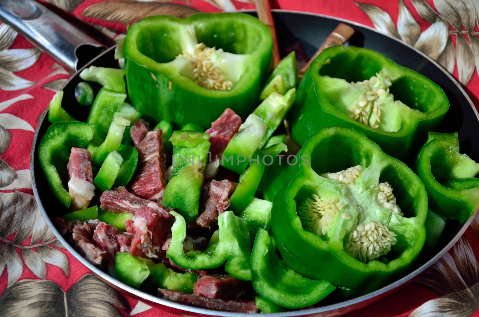 Raw beef slices and green pepper pieces make for the ingredients for pepper steak