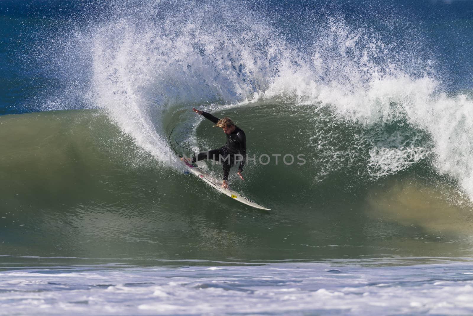 Surfer midway through a strong rail power carve with spray on wave at Jeffreys Bay