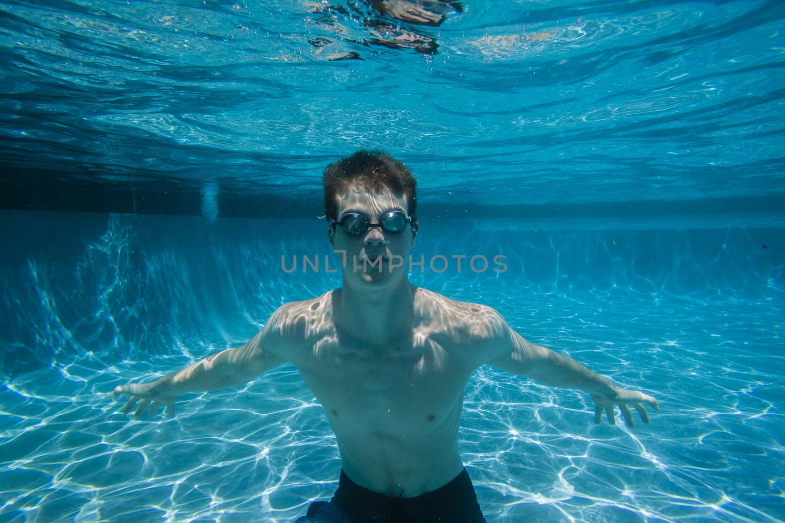 Teenager under water in pool with swim goggles on a summers day