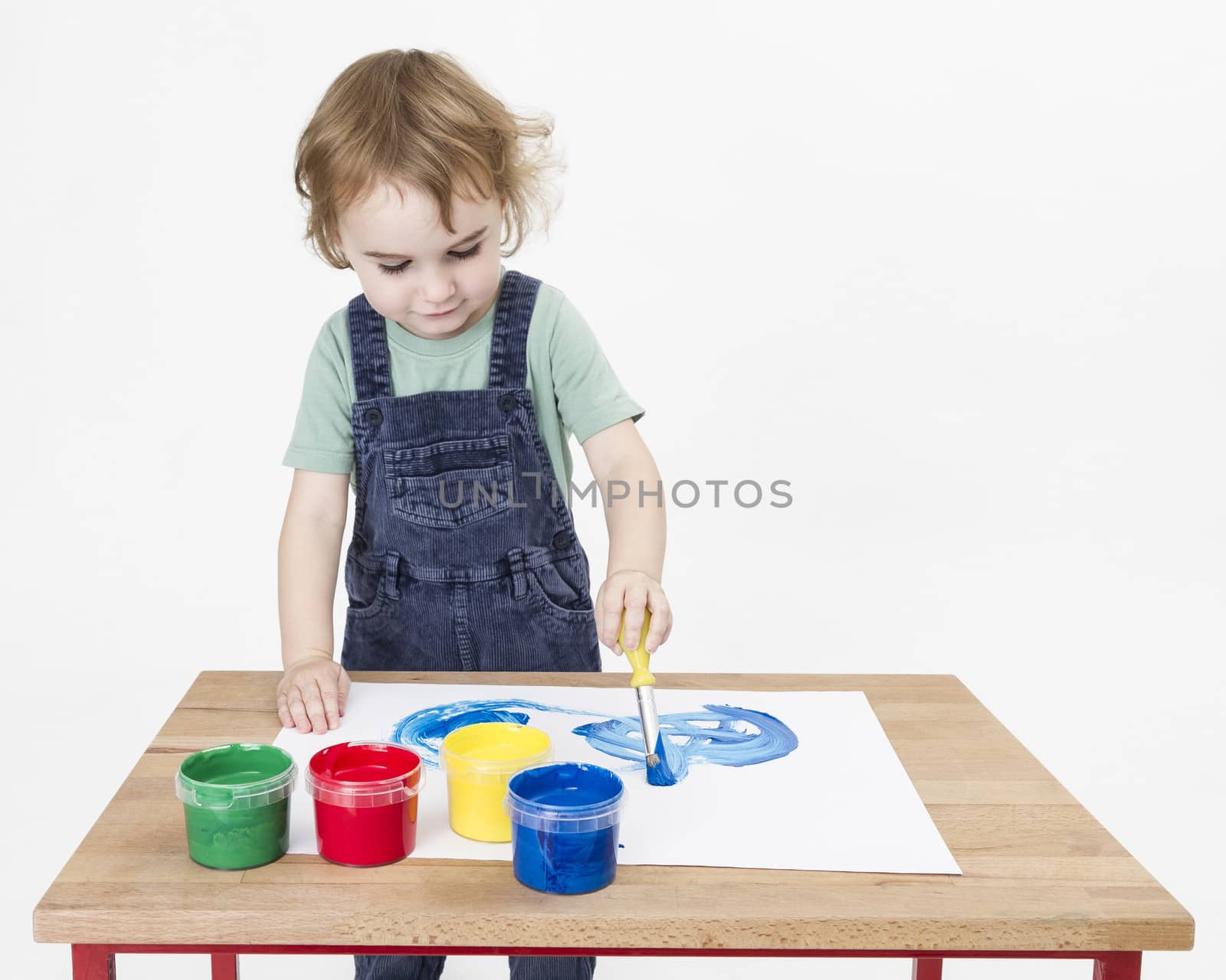 cute girl painting on small desk in grey background. studio shot