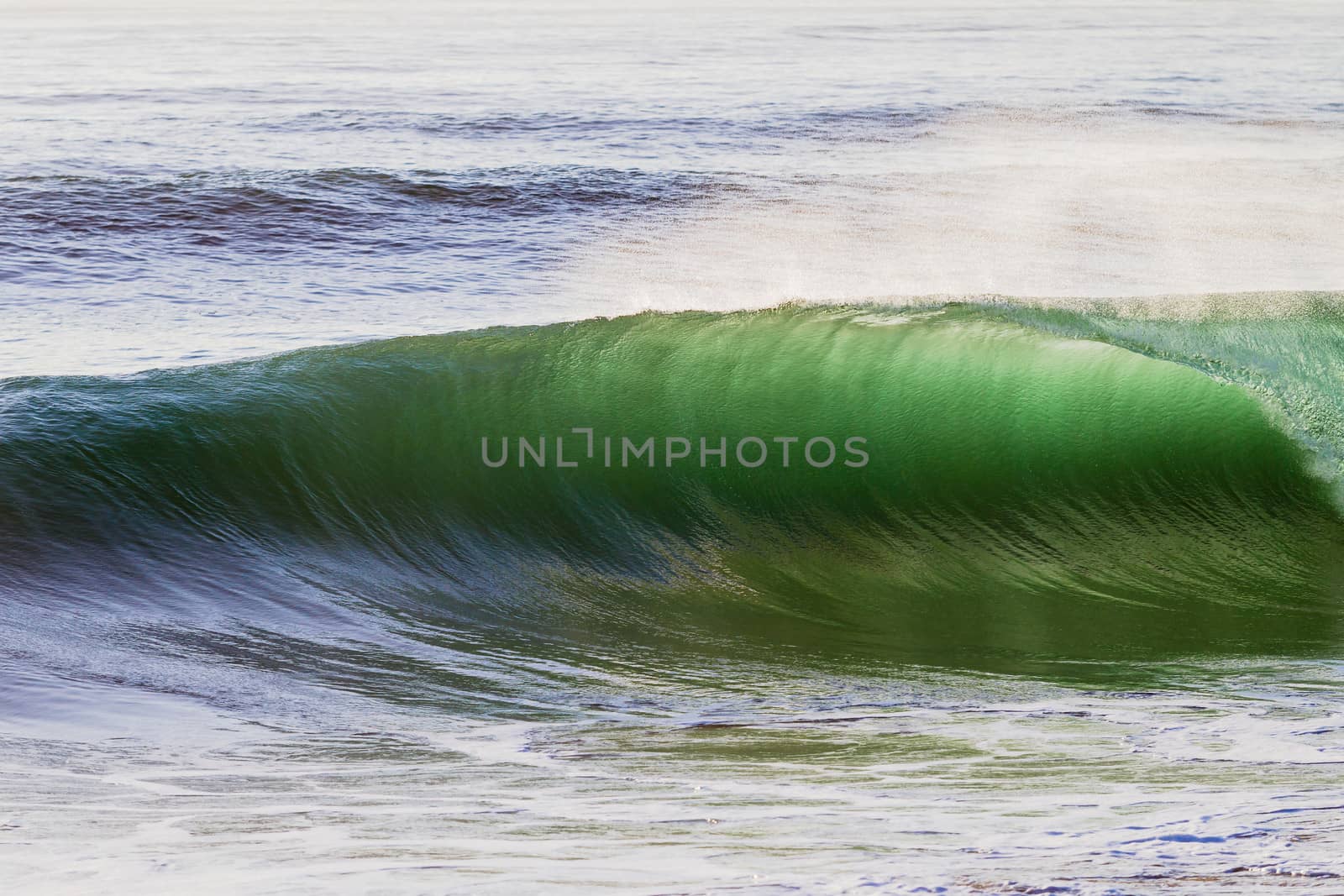 Clean shape ocean wave breaking crashing towards the sandbar shallows backlight.