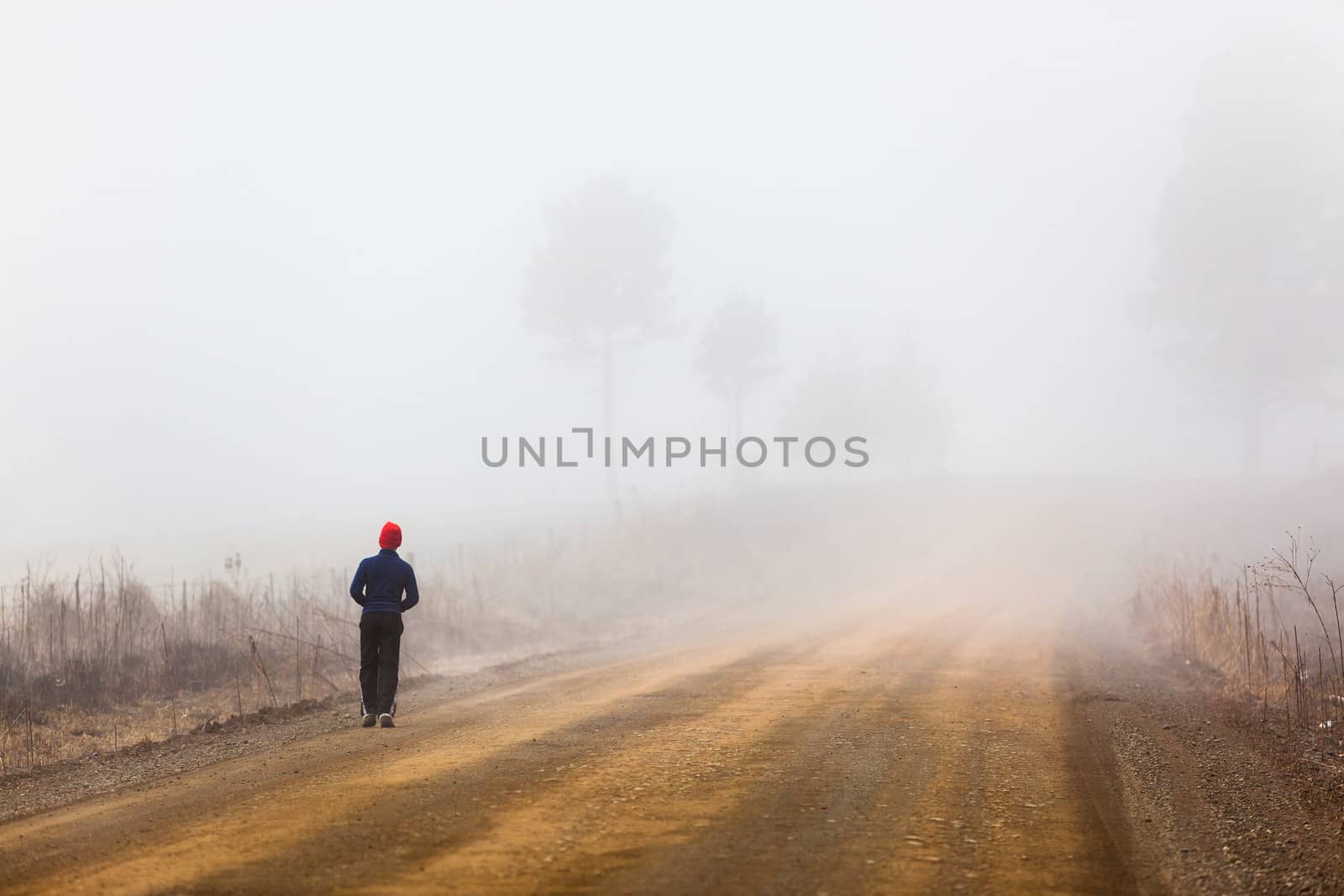 Teenager walking on a mountain dirt road in the morning mist.