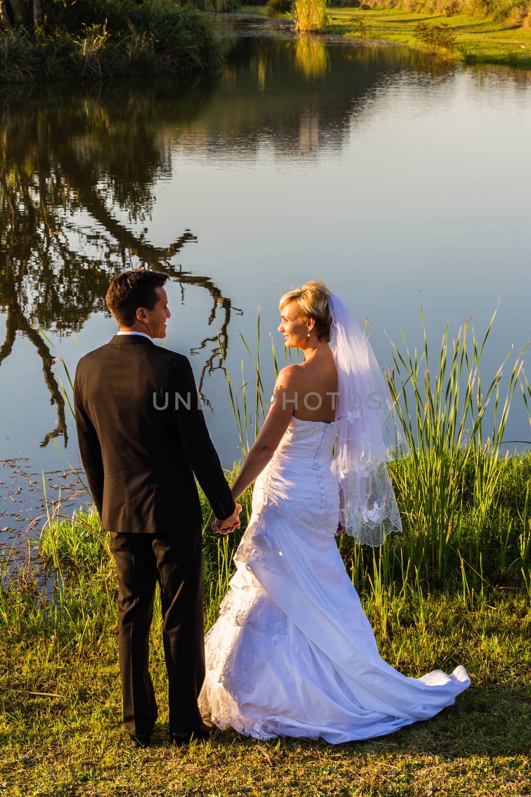 Bride groom now husband wife standing in late summer sunlight by small lake.