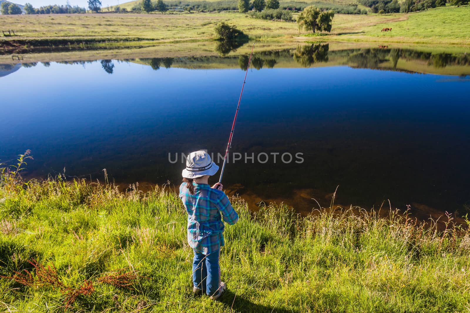 Young girl trout bass fishing in a dam with smooth glass water reflections in the mountains.