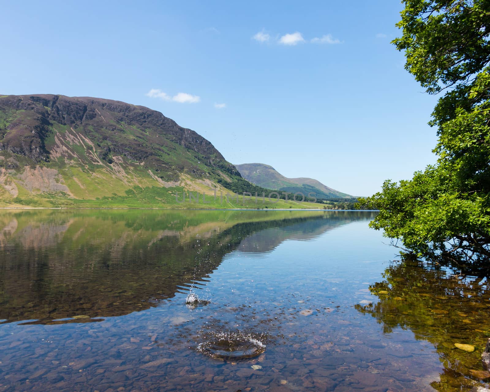 Mirror like reflection of the Lake District hills surrounding Crummock Water with a splash from thrown stone spoiling the smooth surface. Idyllic image from the English Lakes