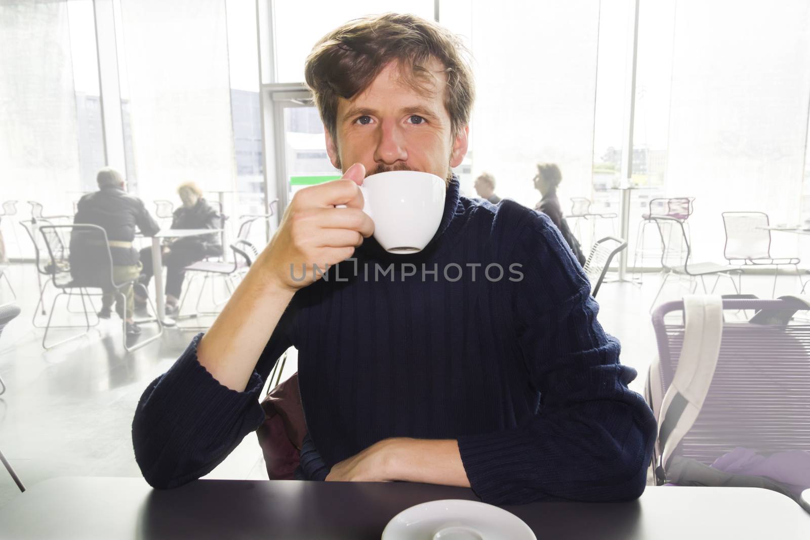 Young man drinking coffee in a cafe by Tetyana
