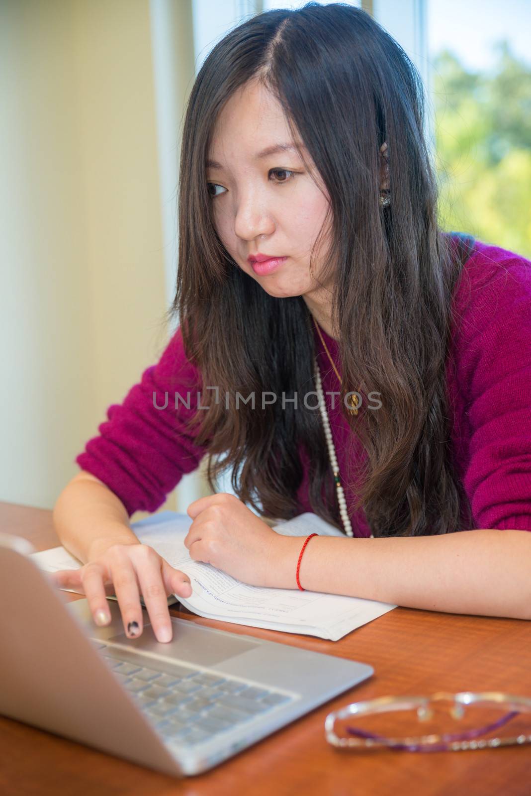 Young woman studying on laptop in front of a large window