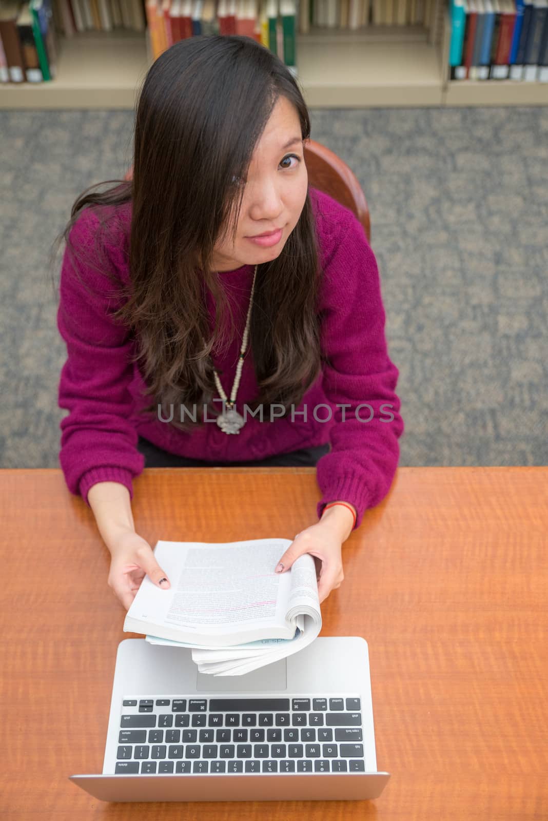 Woman with book and laptob studying in library