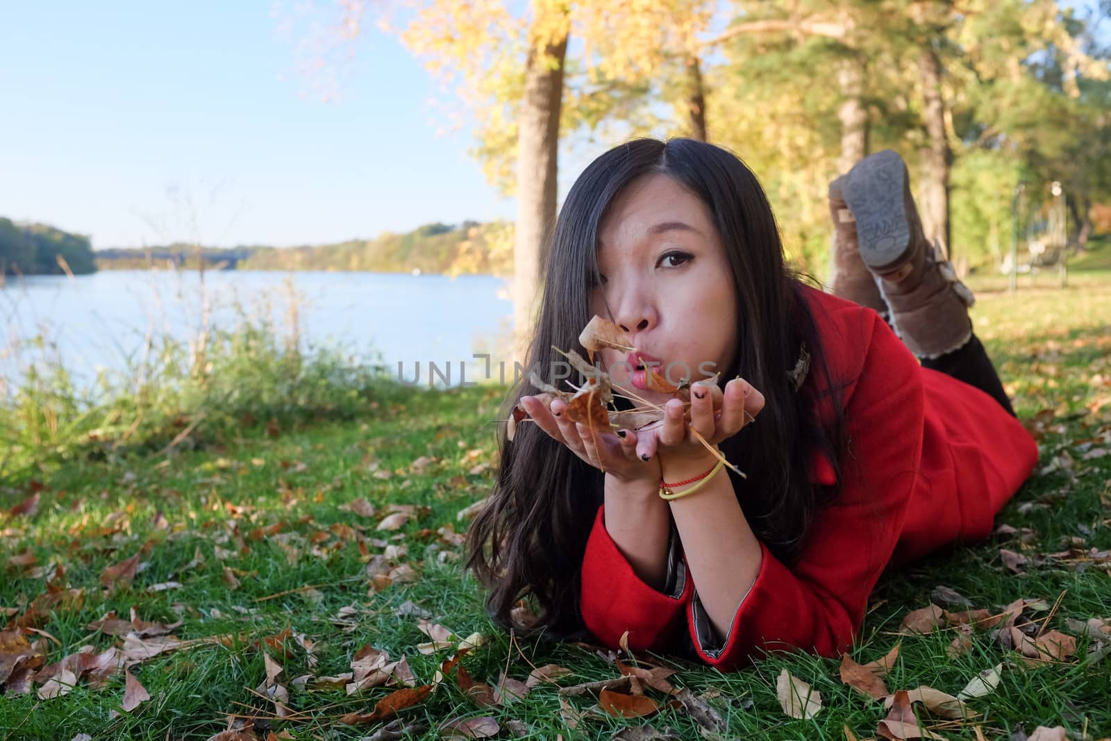 Woman laying on grass blowing away a handful of leaves