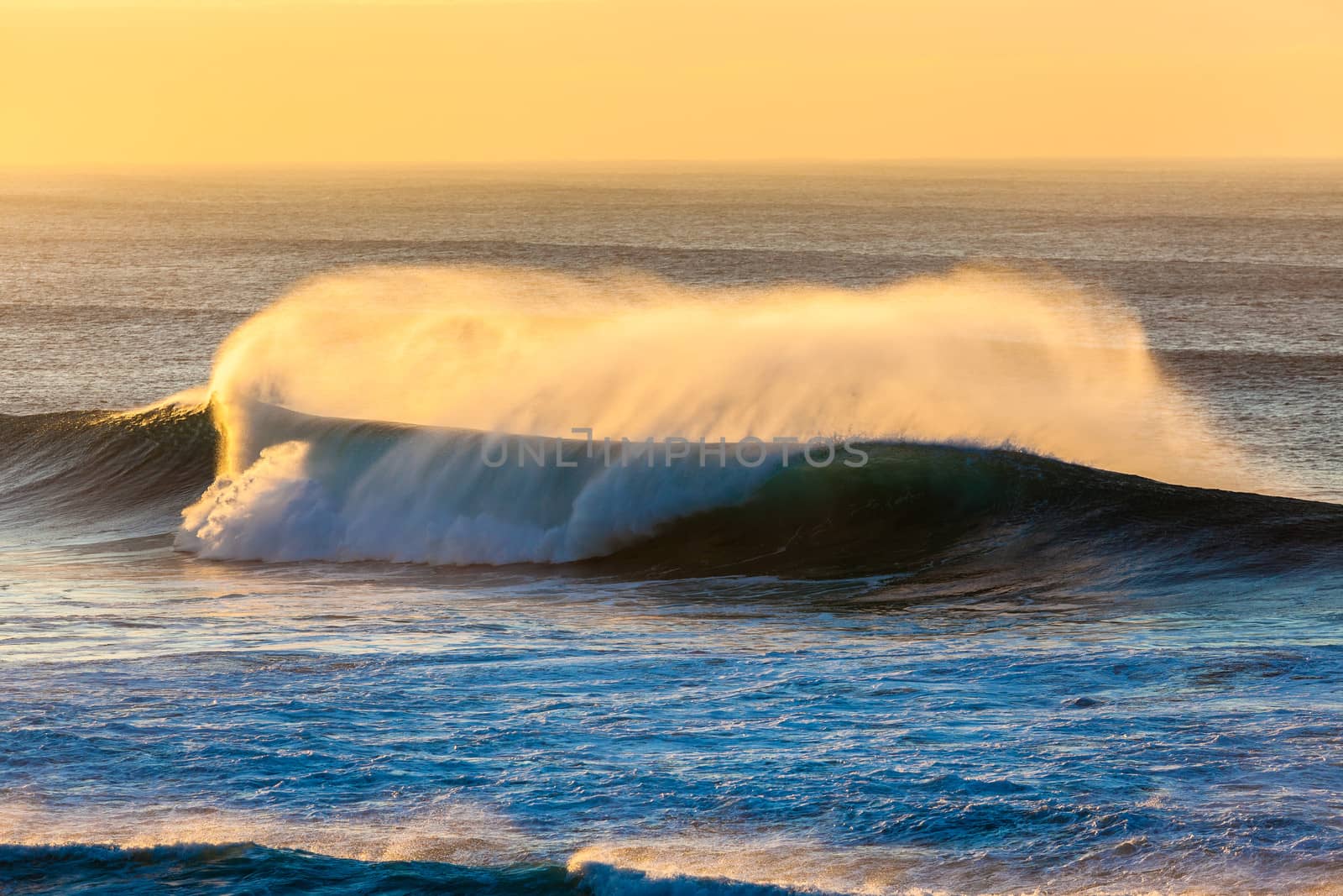 Morning sea wave breaking or crashing onto shallow sandbar reef with offshore wind spray.