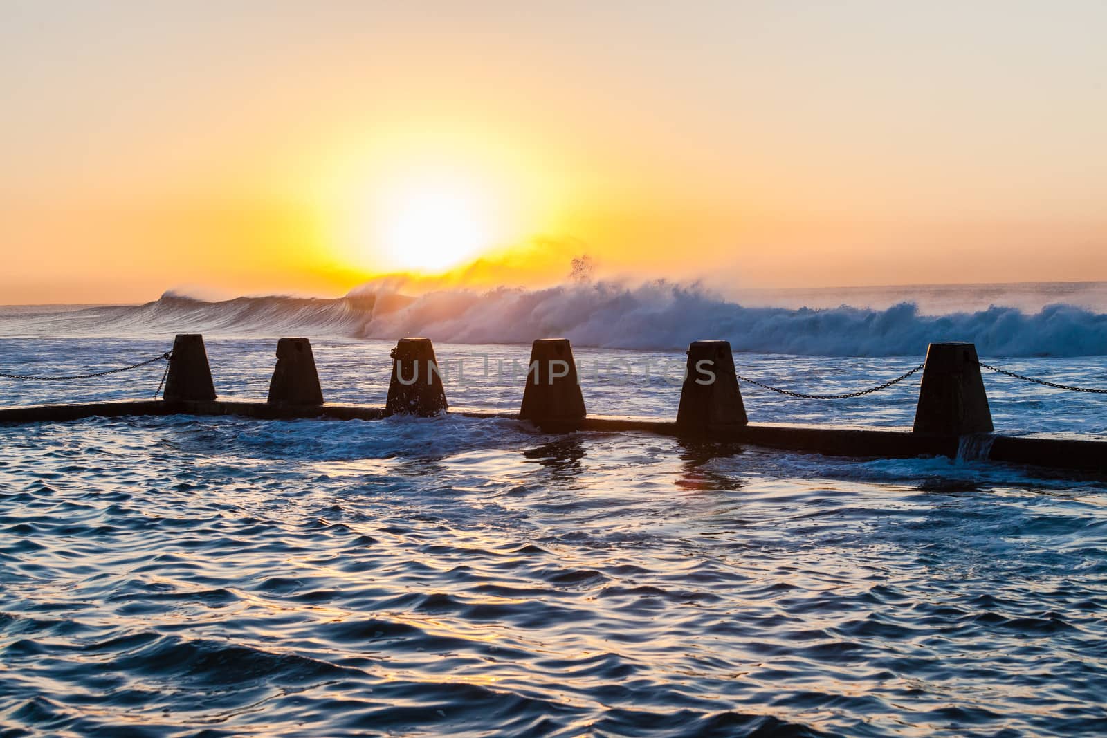 Large ocean wave swells crashing and rolling towards the shoreline and washing into tidal pool at sunrise.