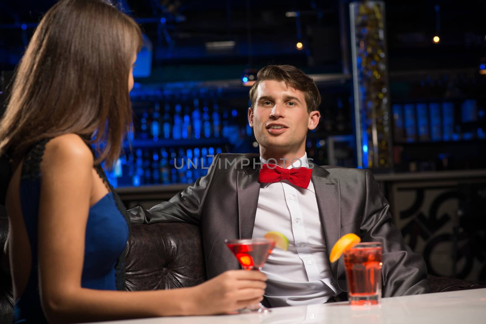 portrait of a man in a nightclub, sitting on the couch and talking with woman