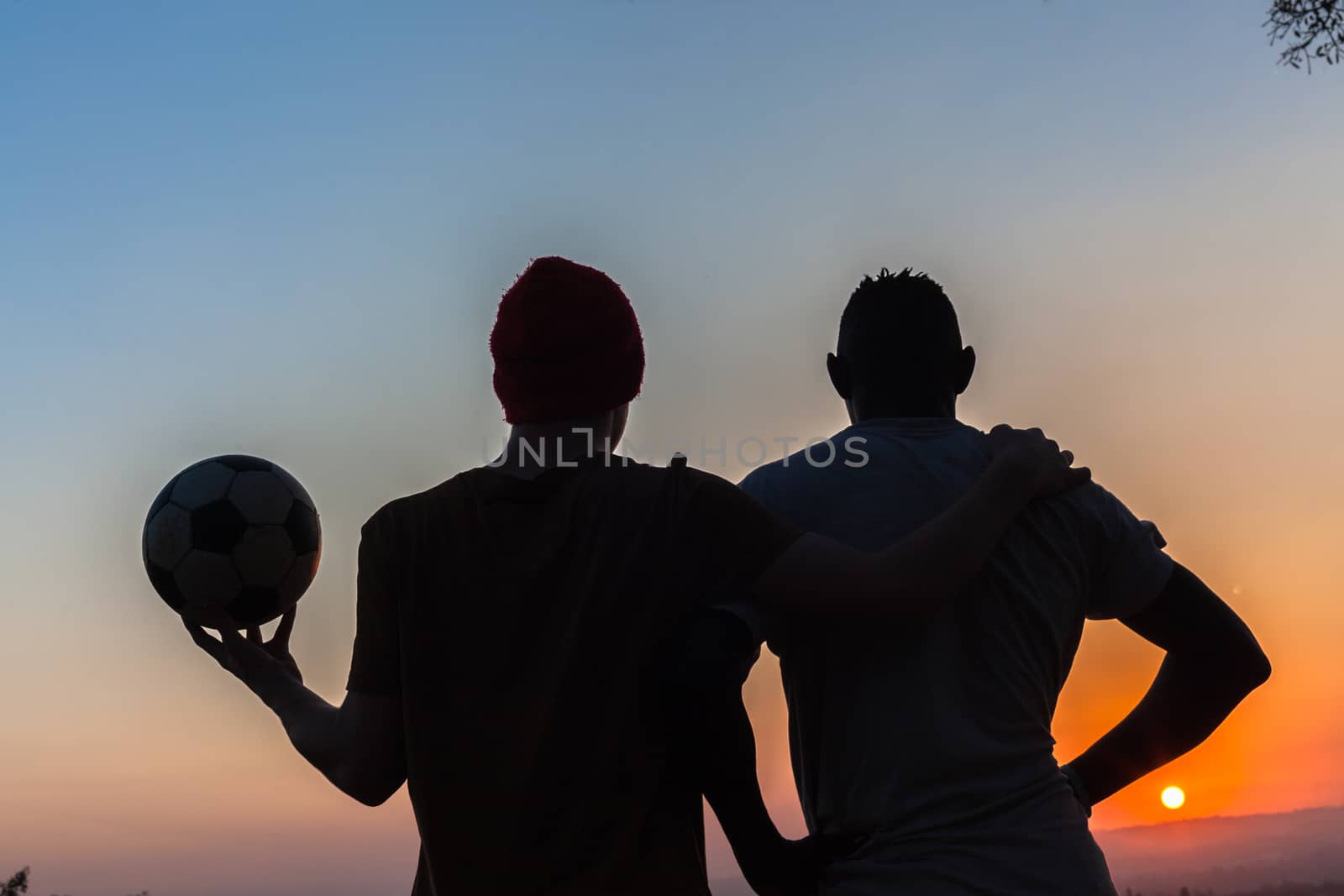Friends body outlines silhouetted watch sunset after playing football.