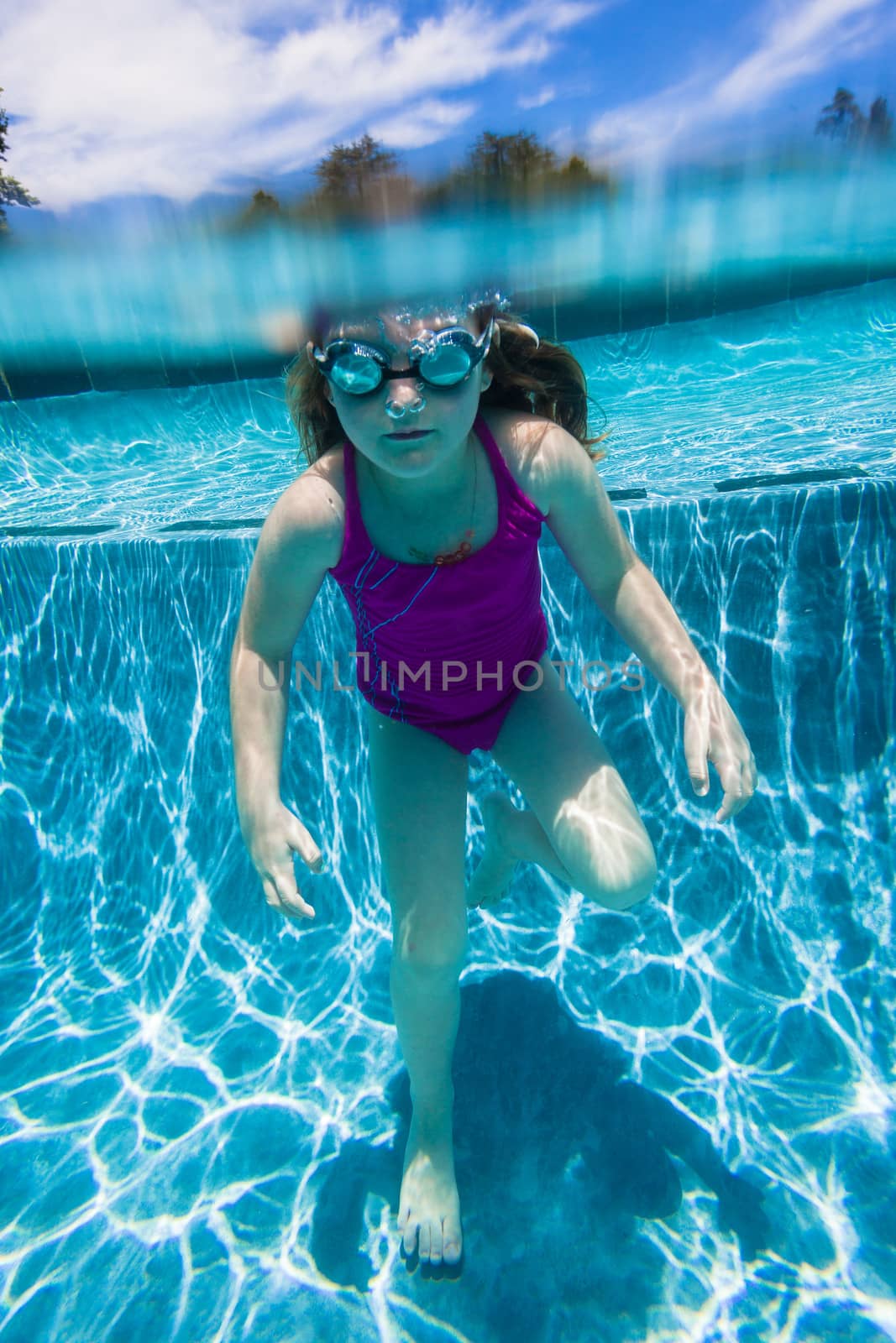 Young girl wearing goggles underwater in swimming pool.