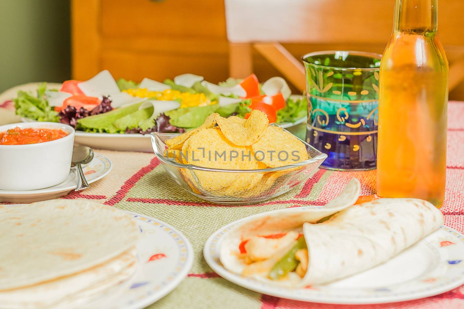 Traditional mexican food in a table, with bowl of nachos, spicy sauce, chicken fajita, tortillas and fresh salad