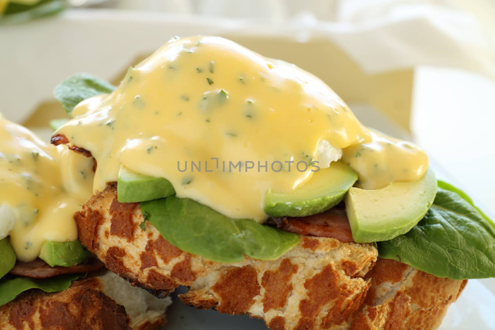 Beautiful eggs benedict with bacon and a rich hollandaise sauce on tiger crust bread.