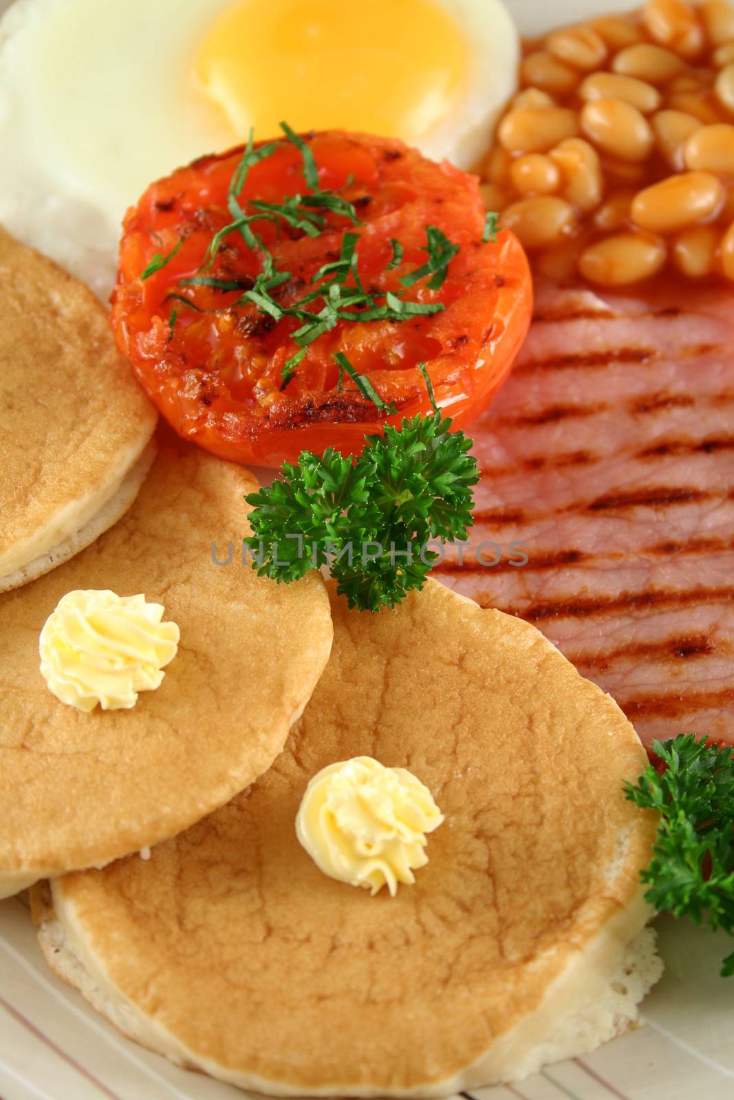 Breakfast of grilled bacon, tomato, egg, baked beans and pancakes.