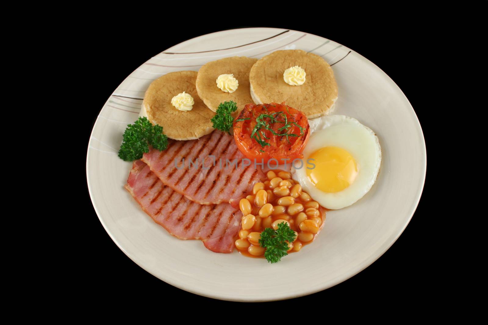 Breakfast of grilled bacon, tomato, egg, baked beans and pancakes.