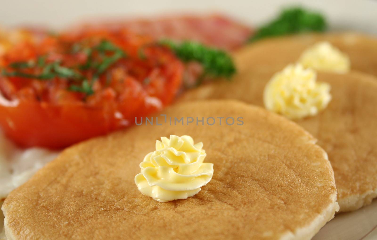 Breakfast of grilled bacon, tomato, egg, baked beans and pancakes.