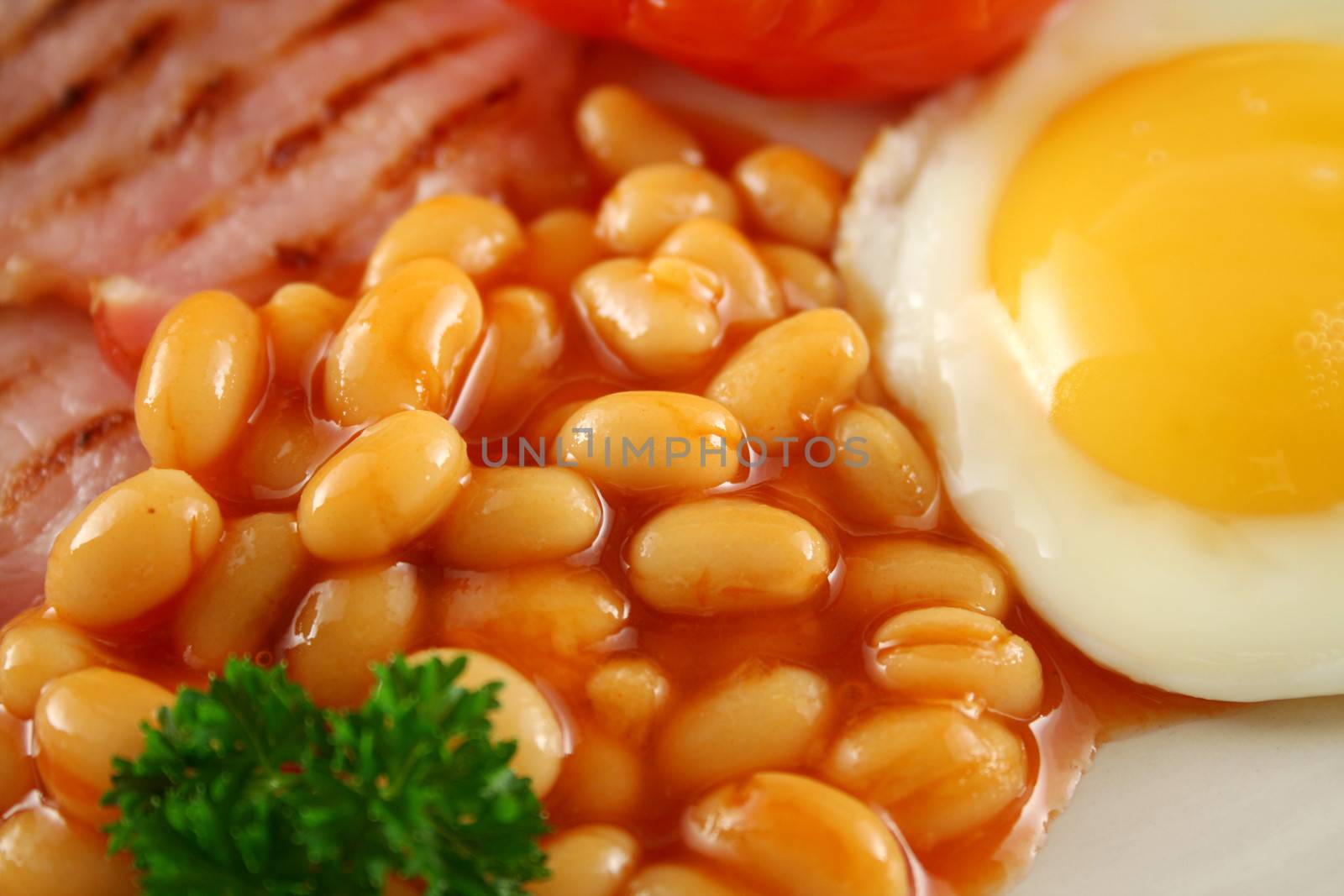 Breakfast of grilled bacon, tomato, egg, baked beans and pancakes.