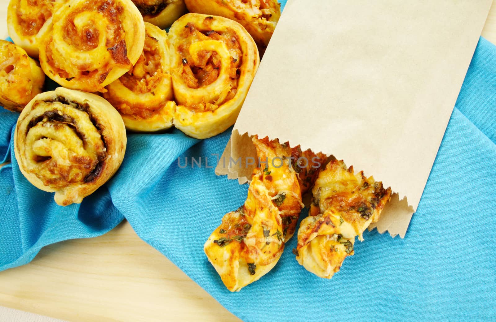 A selection of baked treats including tomato and herb sticks in a paper bag and baked scrolls.