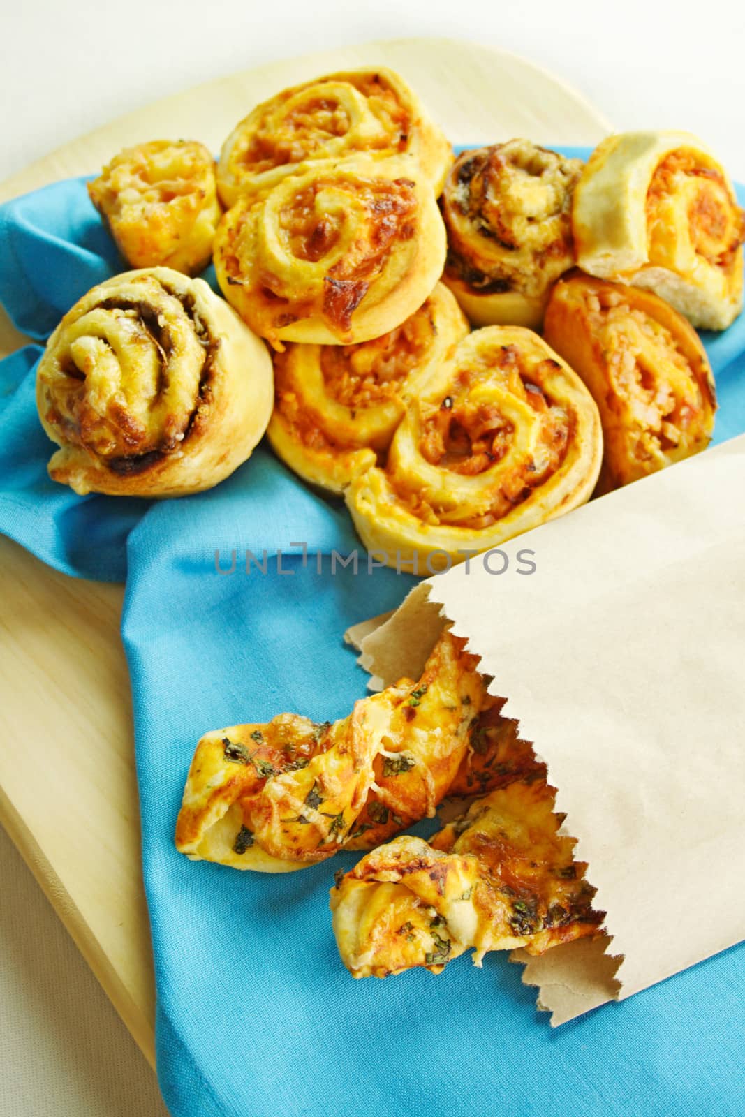 A selection of baked treats including tomato and herb sticks in a paper bag and baked scrolls.