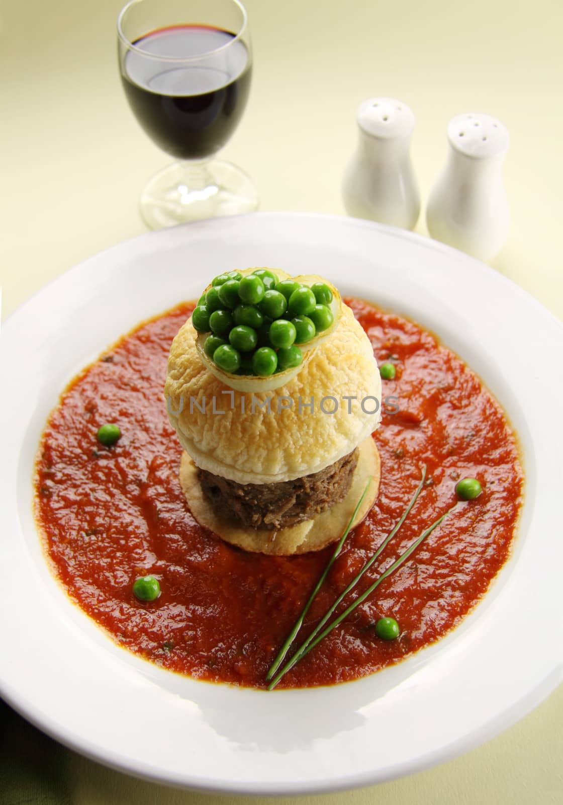 Tall beef pie with peas floating in tomato sauce.