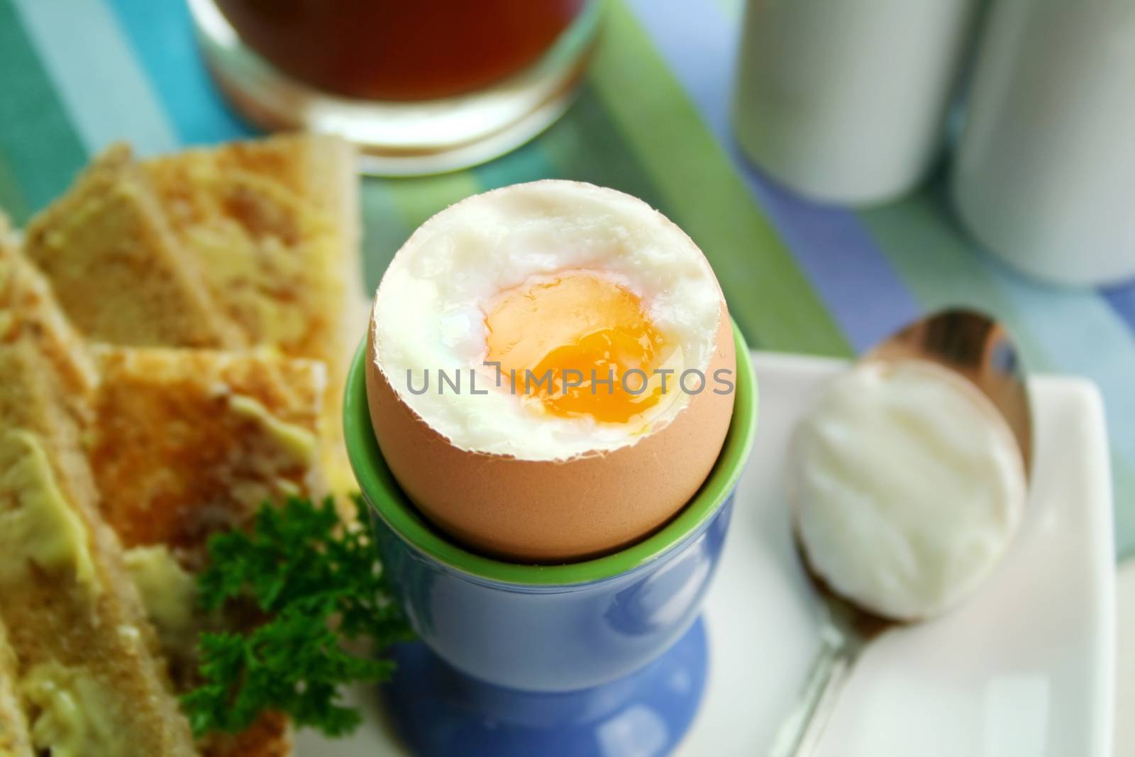 Breakfast of a boiled egg, toast fingers and tomato juice.